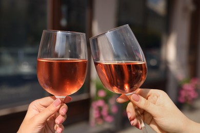 Photo of Women clinking glasses with rose wine outdoors, closeup