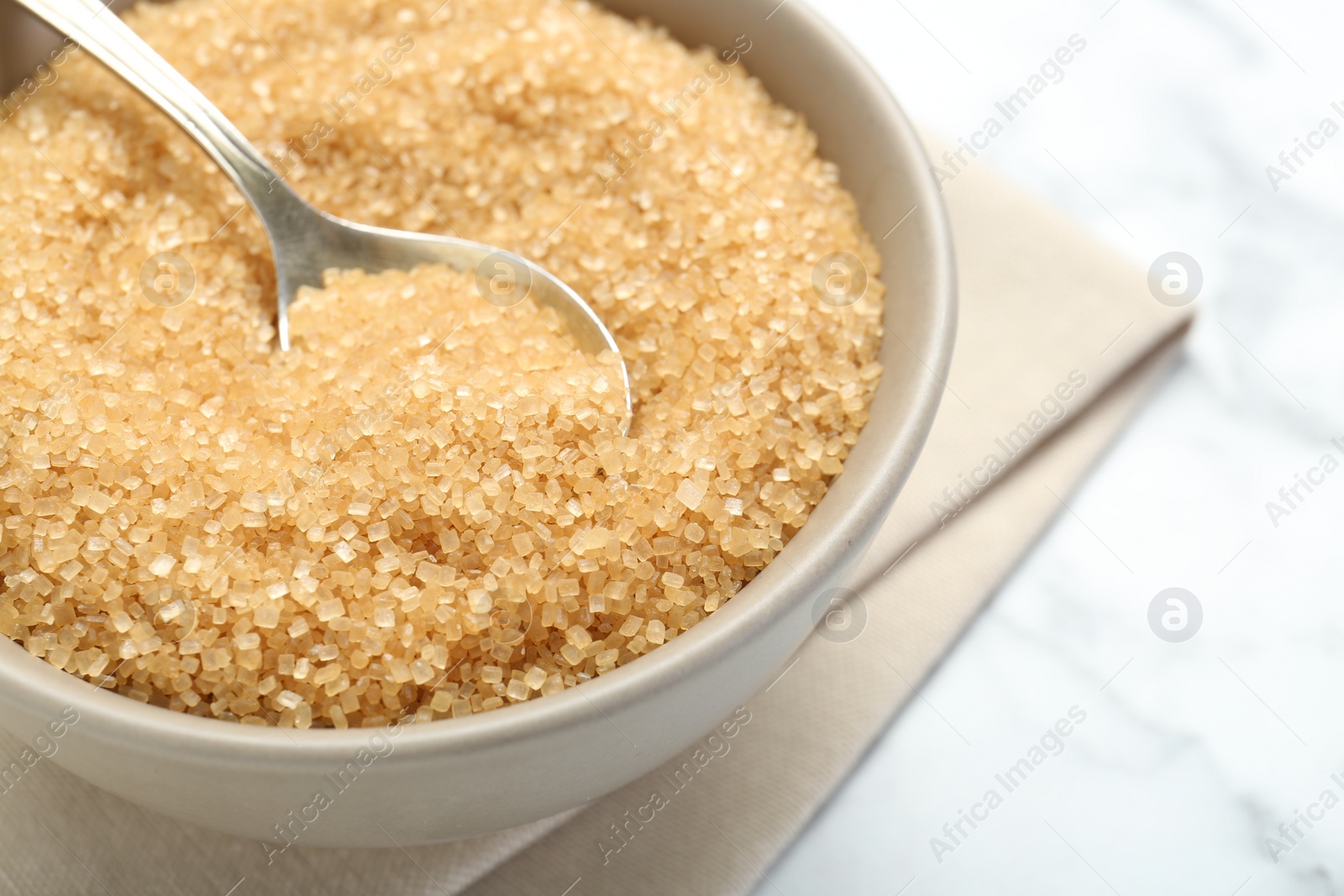 Photo of Brown sugar in bowl and spoon on white marble table, closeup. Space for text