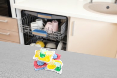 Dishwasher detergent pods and tablets on grey wooden table in kitchen