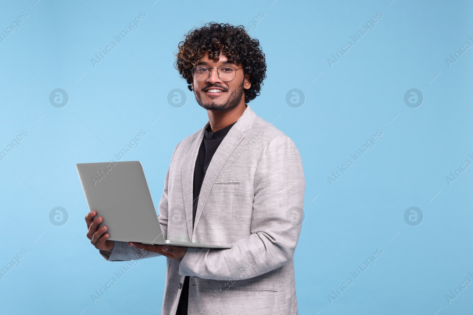 Photo of Smiling man with laptop on light blue background. Space for text