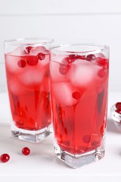 Tasty cranberry juice with ice cubes in glasses on white wooden table