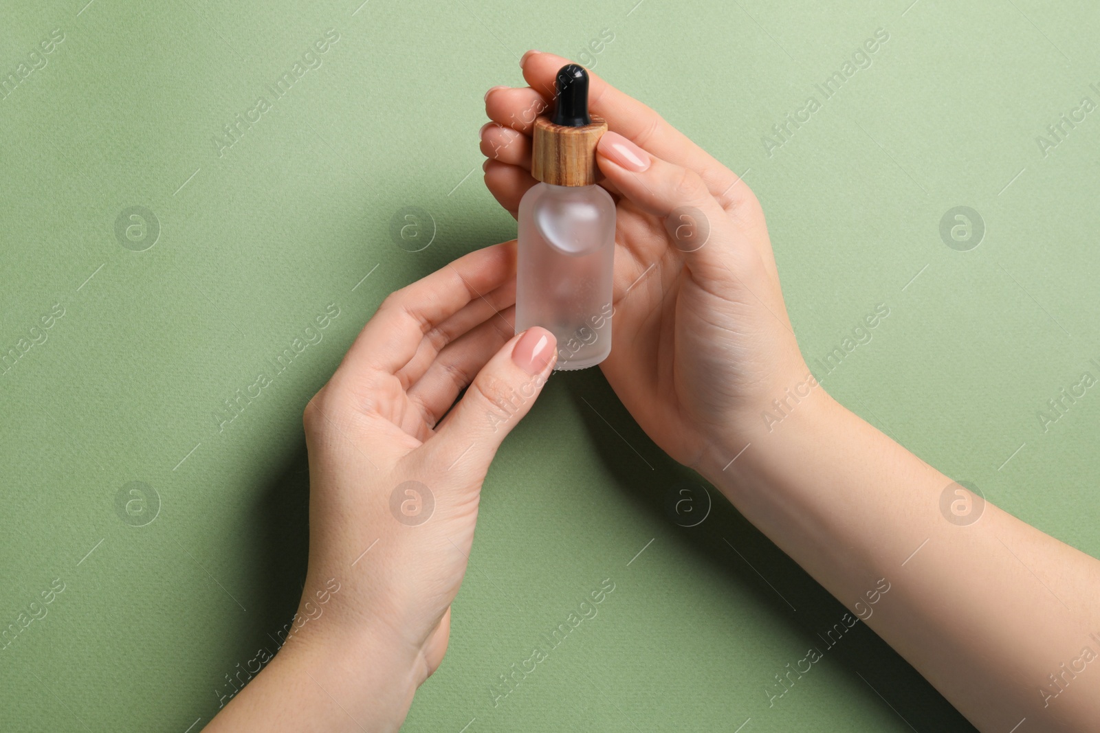Photo of Woman holding bottle with serum on olive background, closeup