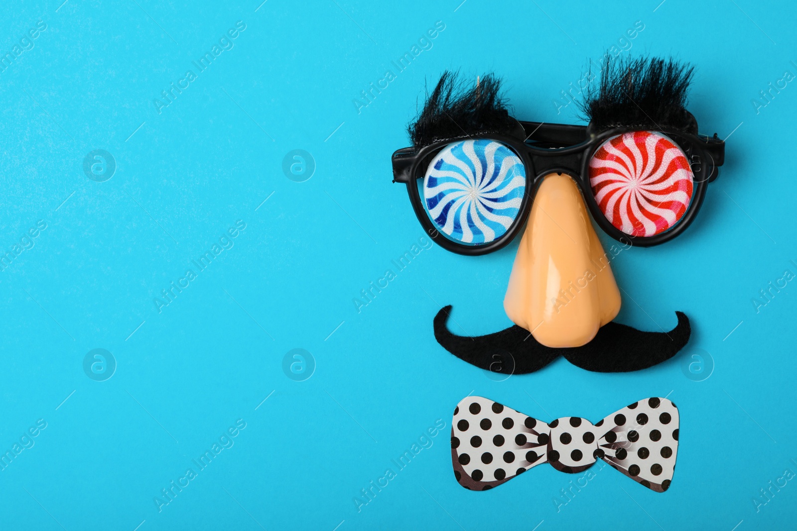 Photo of Funny party glasses and space for text on light blue background, flat lay. April Fool's Day