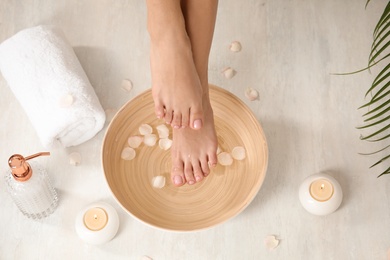 Photo of Woman holding her feet over bowl with water and rose petals on floor, closeup. Spa treatment