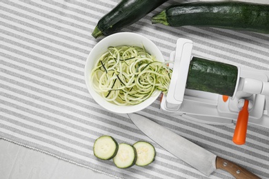 Photo of Making zucchini noodles with spiral slicer on table, flat lay