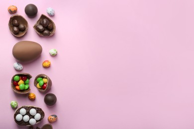 Tasty chocolate eggs and candies on pink background, flat lay. Space for text