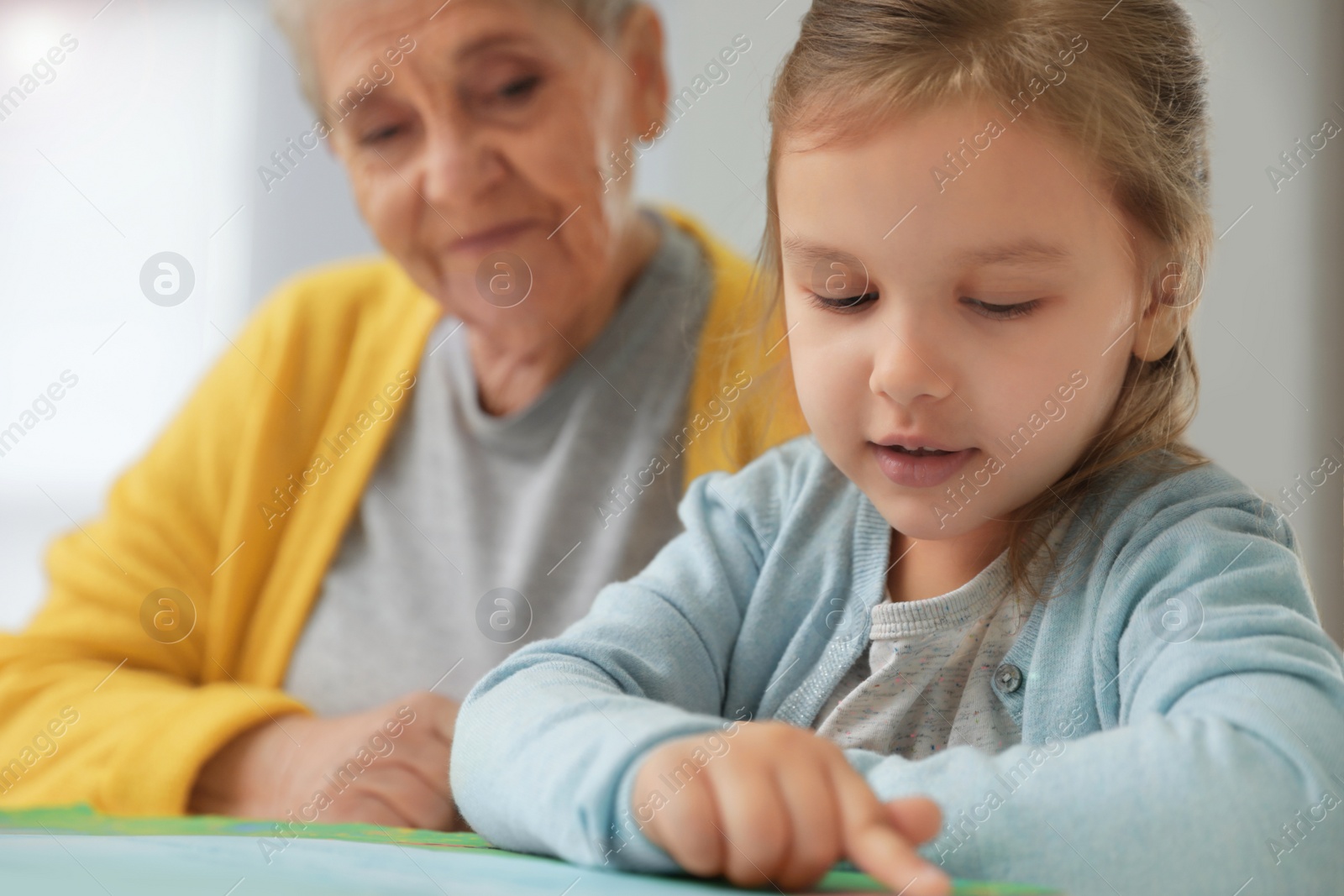 Photo of Cute girl and her grandmother reading book at home