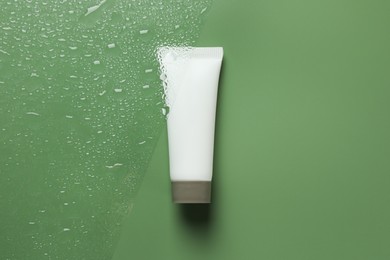Photo of Tube with moisturizing cream on wet green surface, top view