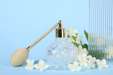 Photo of Aromatic perfume in bottle and beautiful jasmine flowers on light blue background, closeup