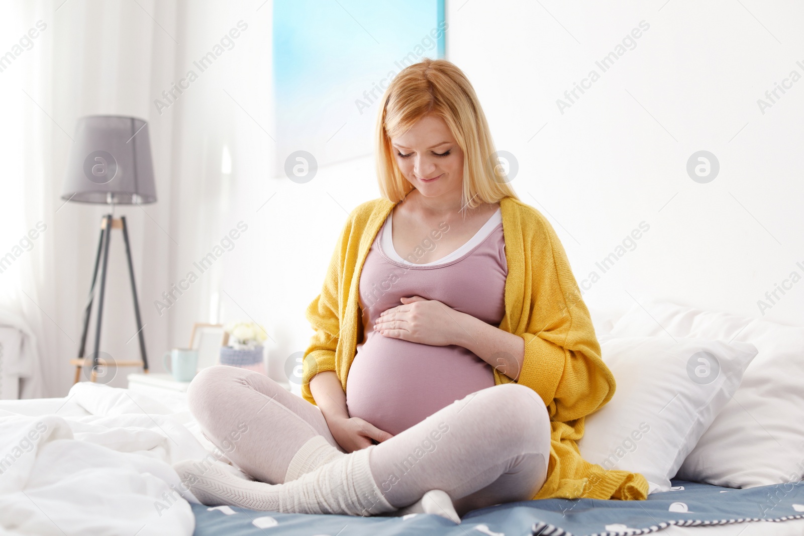 Photo of Beautiful pregnant woman sitting on bed in light room