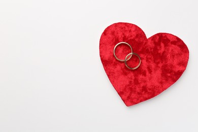 Honeymoon concept. Red velvet heart and two golden rings on white background, top view. Space for text