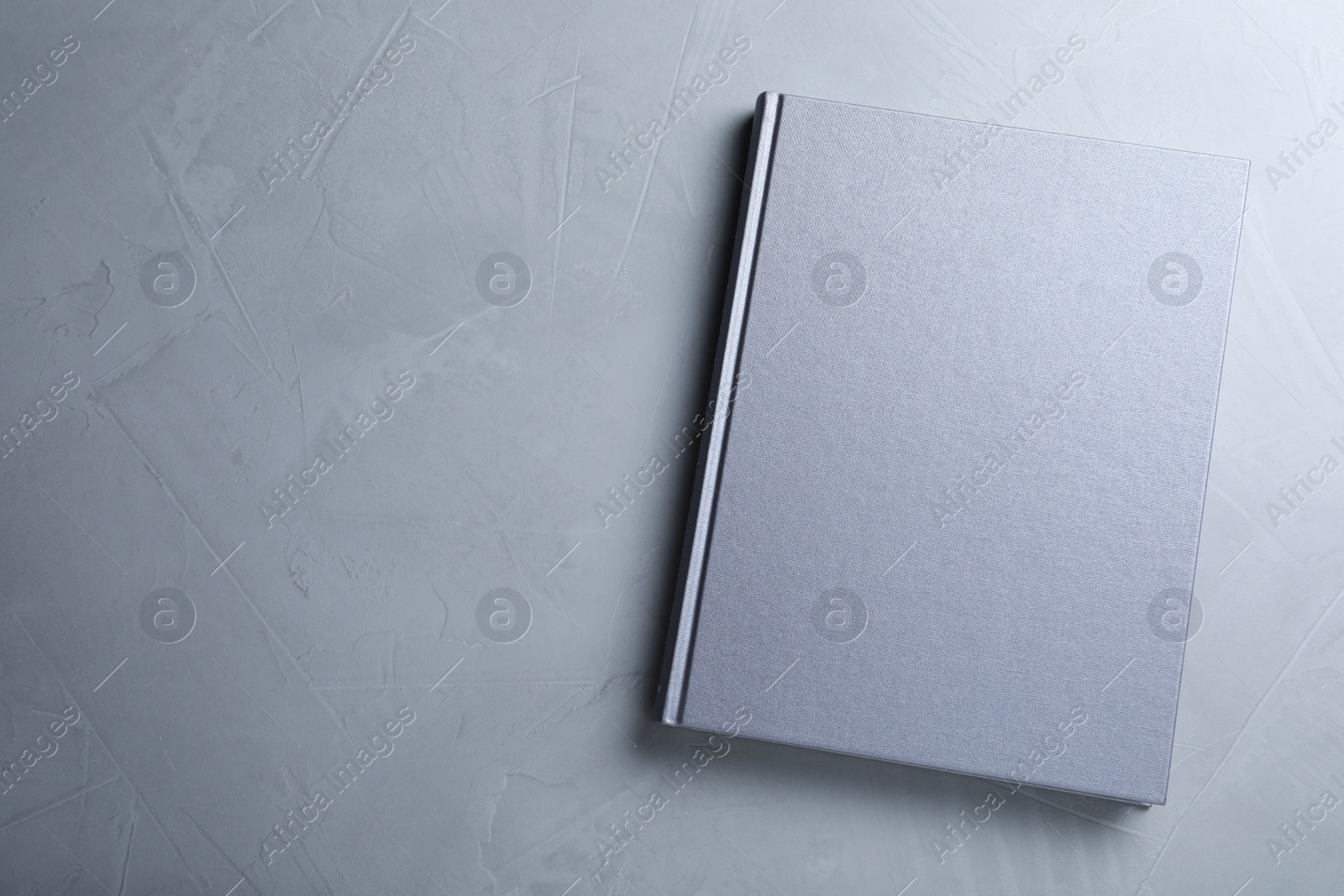 Photo of Closed book with hard cover on grey table, top view. Space for text