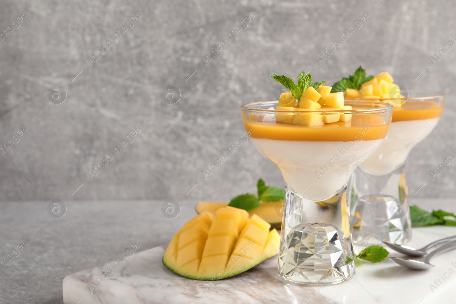 Photo of Delicious panna cotta with mango coulis served on light grey table. Space for text