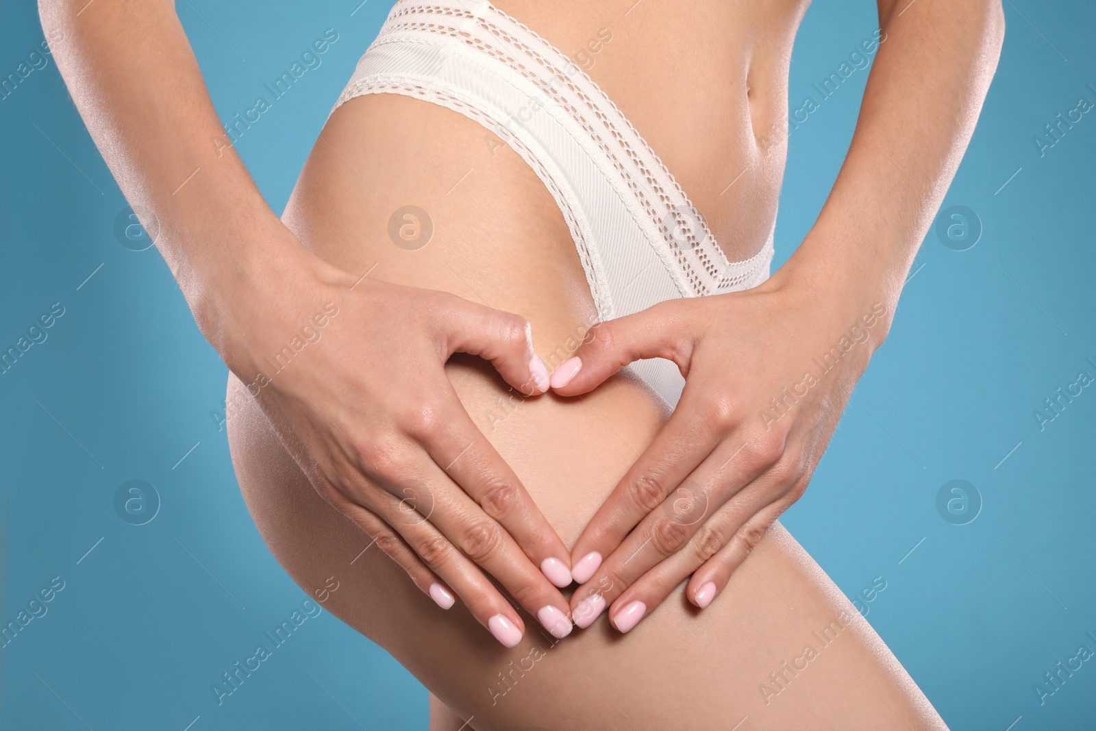 Photo of Closeup view of slim woman in underwear showing heart on light blue background. Cellulite problem concept