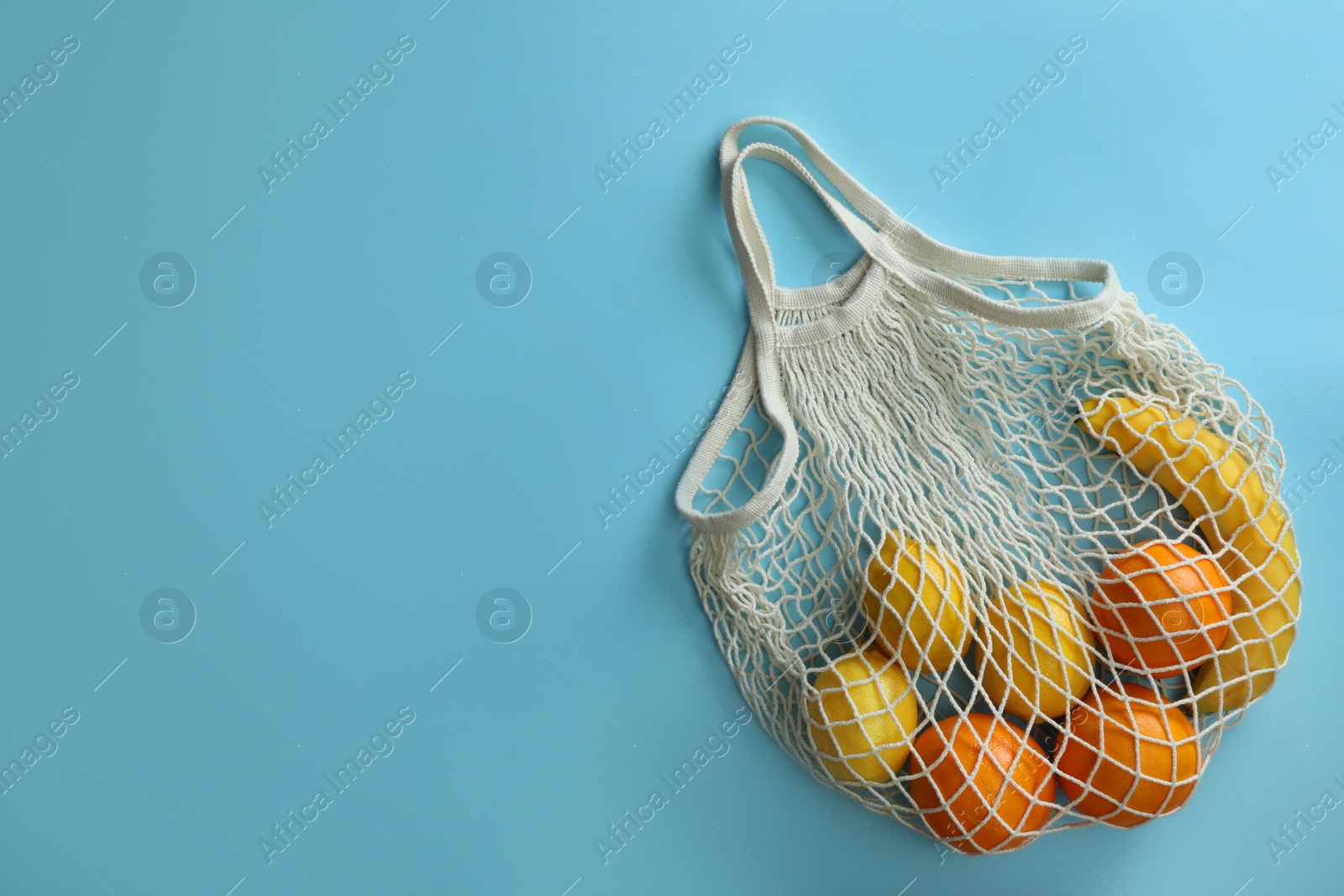 Photo of Net bag with fruits on light blue background, top view. Space for text