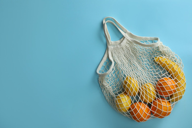 Net bag with fruits on light blue background, top view. Space for text