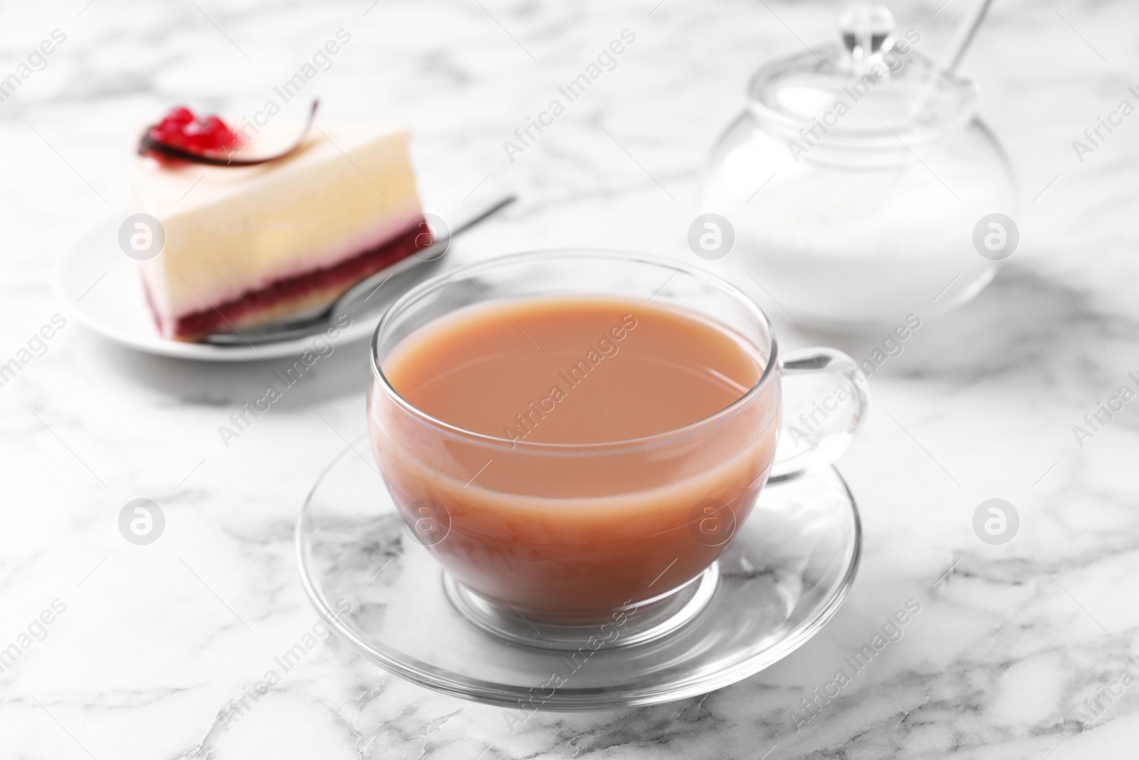 Photo of Delicious tea with milk in glass cup near dessert on white marble table