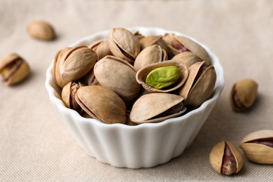 Photo of Bowl and pistachio nuts on beige tablecloth, closeup