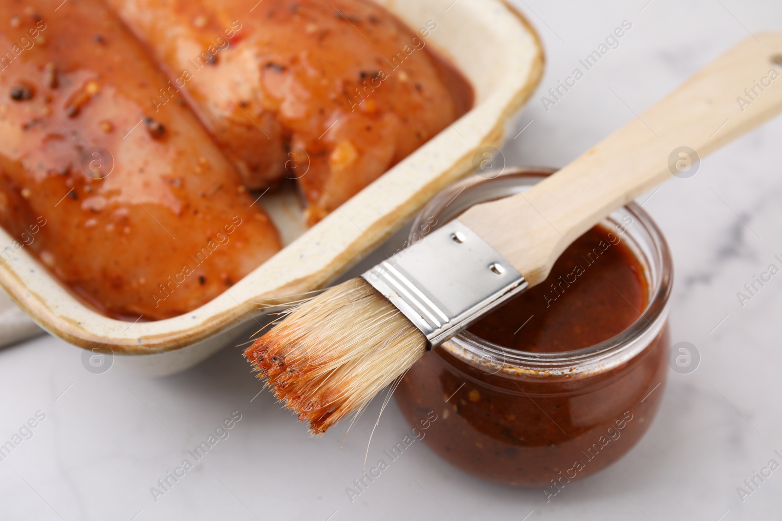 Photo of Fresh marinade, basting brush and raw chicken fillets on white table, closeup