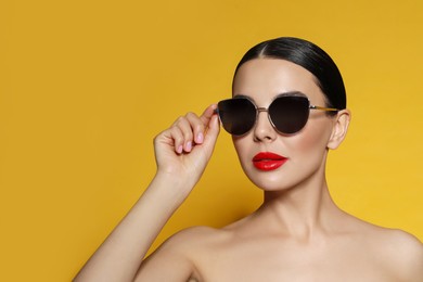 Photo of Attractive woman in fashionable sunglasses against orange background. Space for text