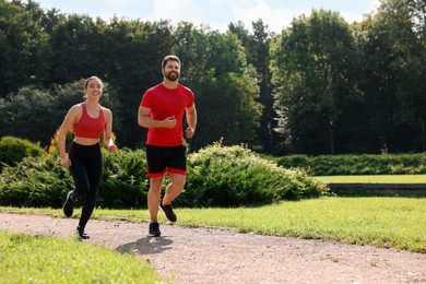 Healthy lifestyle. Happy couple running in park on sunny day, space for text