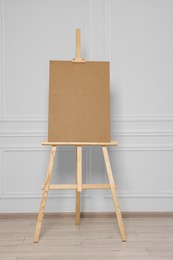 Photo of Wooden easel with blank board near white wall indoors