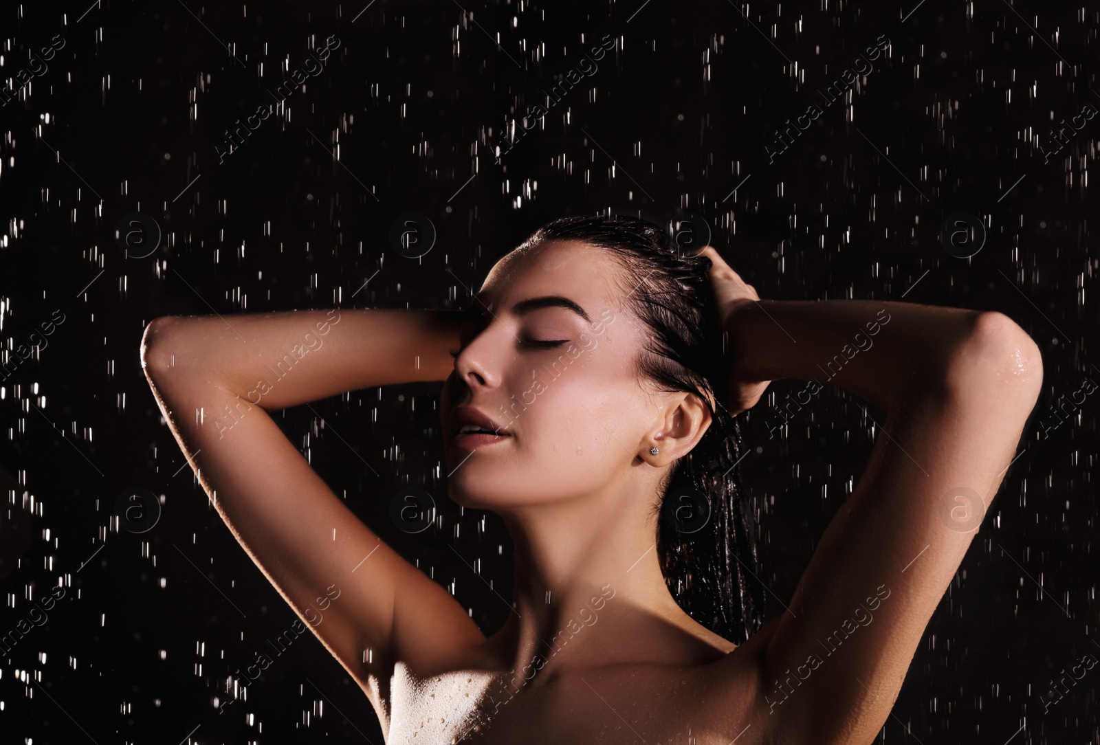 Photo of Young woman washing hair while taking shower on black background