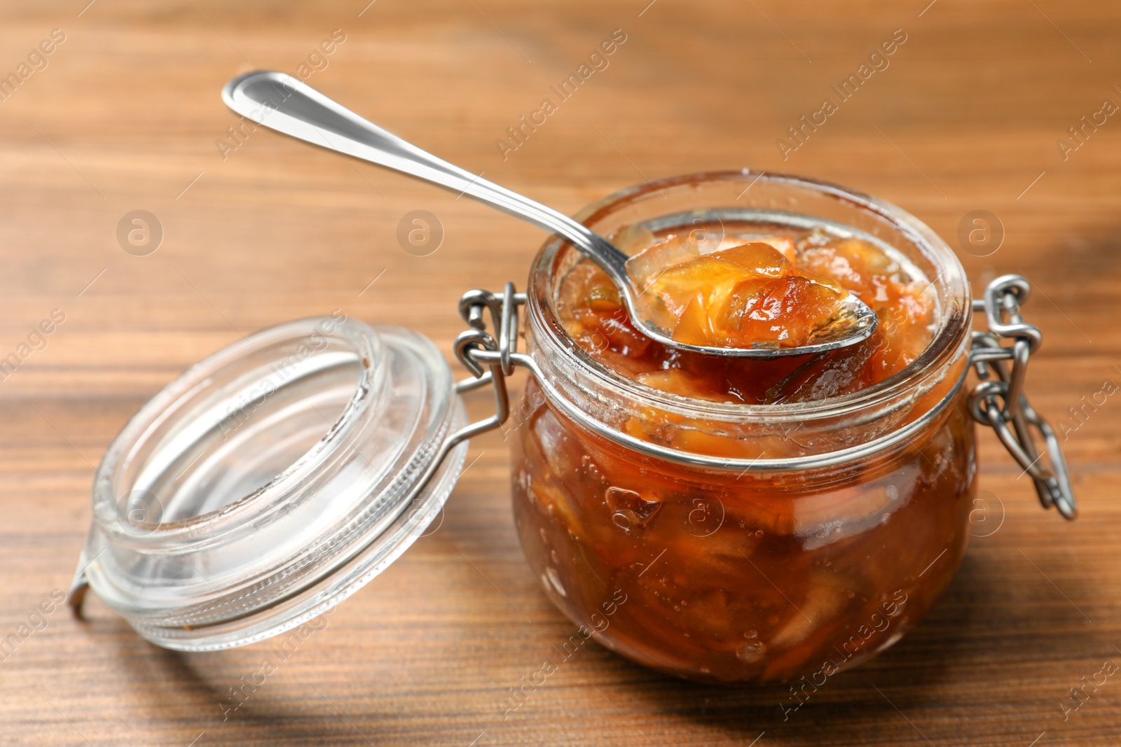 Photo of Tasty apple jam and spoon in glass jar on wooden table, closeup