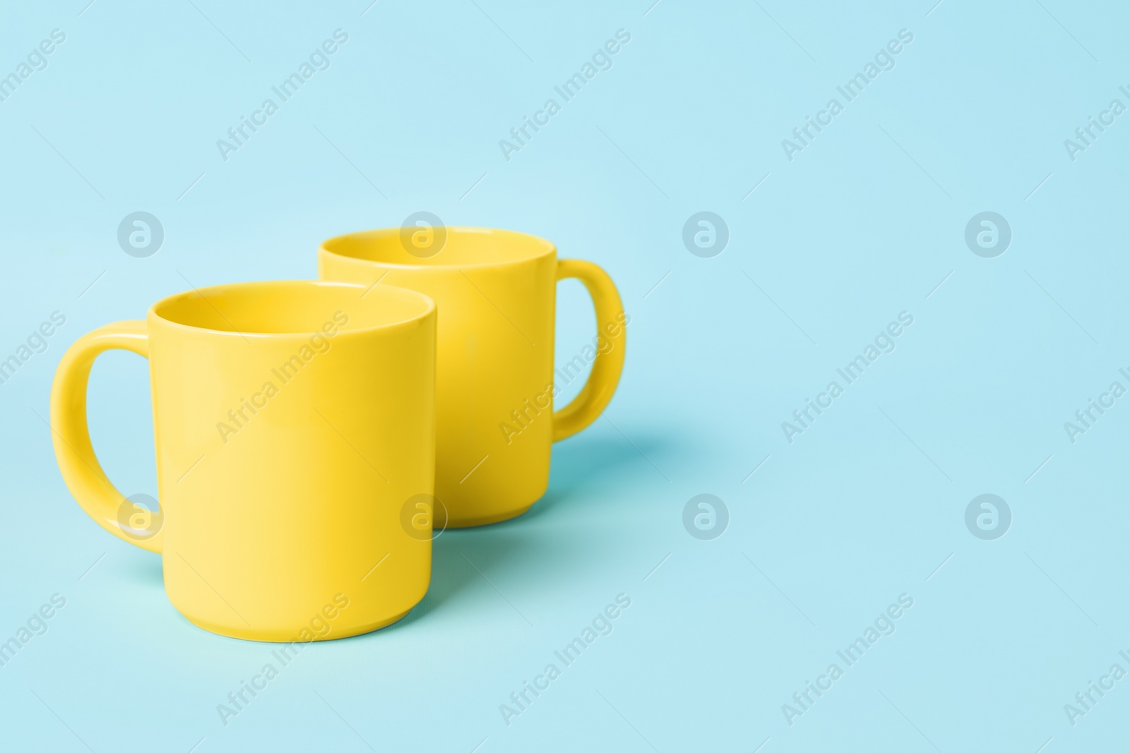 Photo of Two yellow ceramic mugs on light blue background, space for text