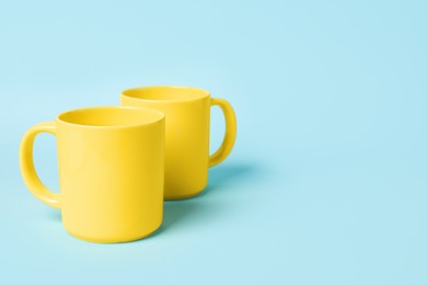 Photo of Two yellow ceramic mugs on light blue background, space for text