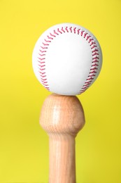 Photo of White ball on wooden baseball bat against yellow background, closeup. Sports equipment