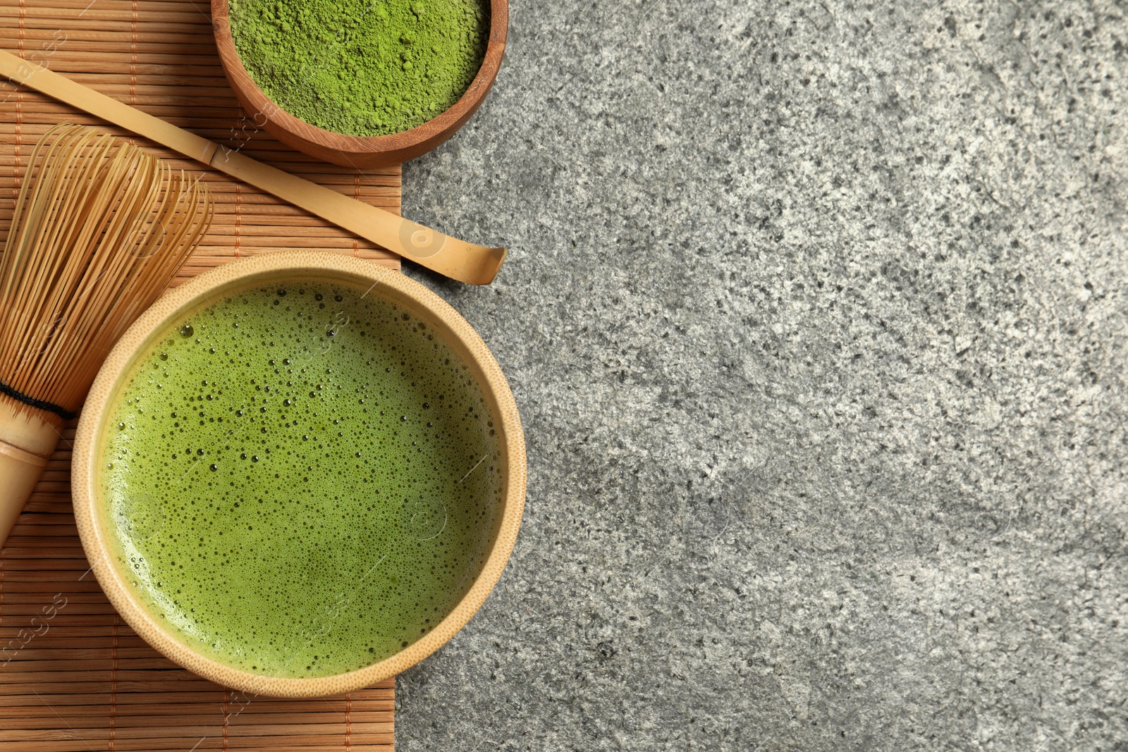 Photo of Cup of fresh matcha tea, bamboo whisk, spoon and green powder on grey table, flat lay. Space for text