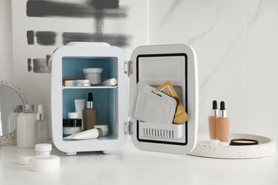 Photo of Cosmetics refrigerator and skin care products on white table indoors