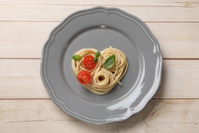 Photo of Heart made of tasty spaghetti, tomato and basil on wooden table, top view