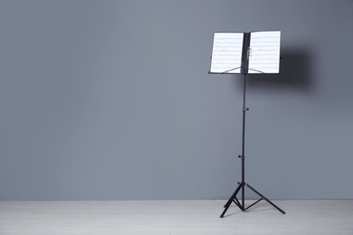 Photo of Note stand with music sheets near grey wall indoors. Space for text