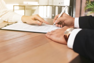 Image of Man signing document at wooden table in office, closeup. Insurance concept