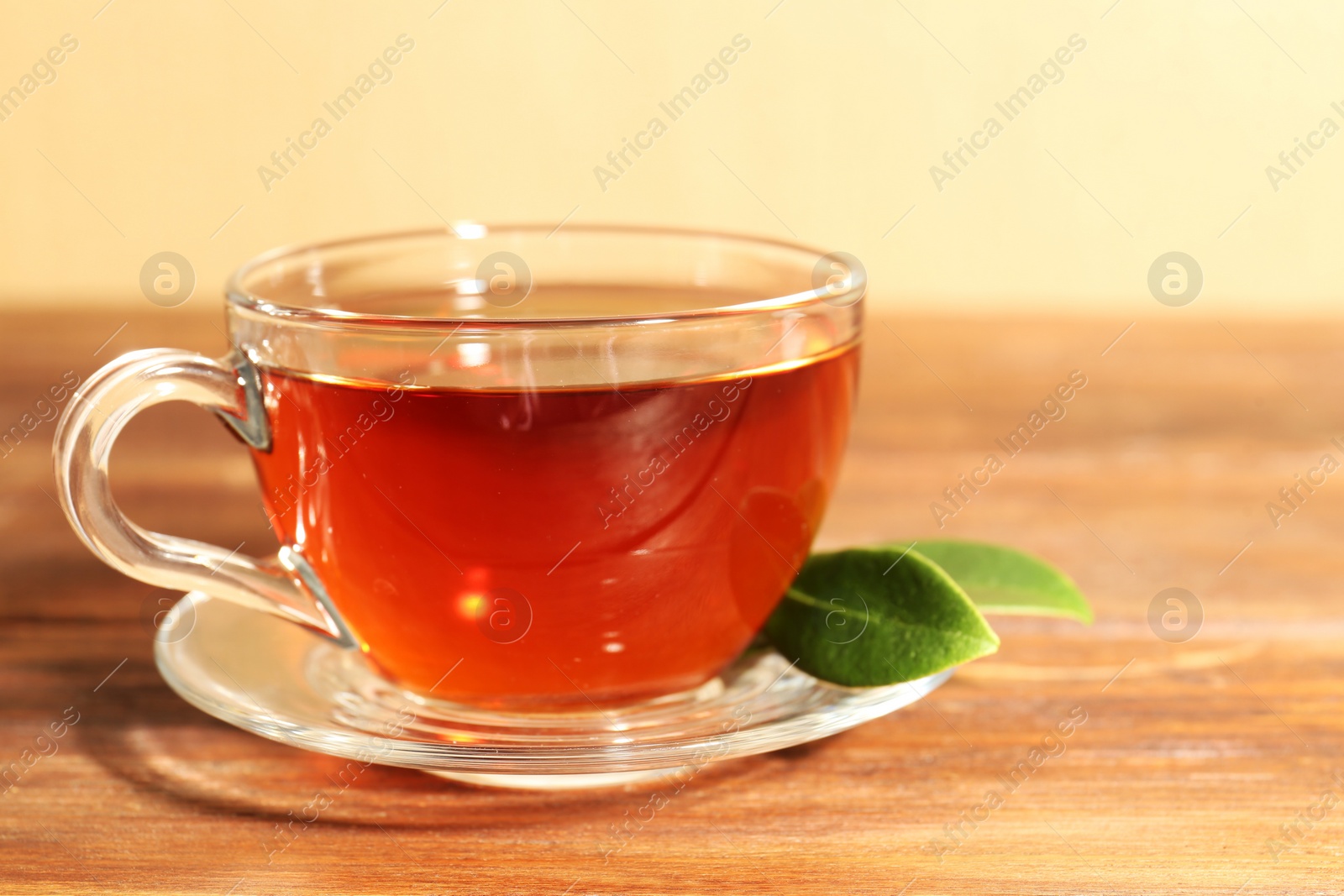 Photo of Aromatic tea in glass cup and green leaves on wooden table