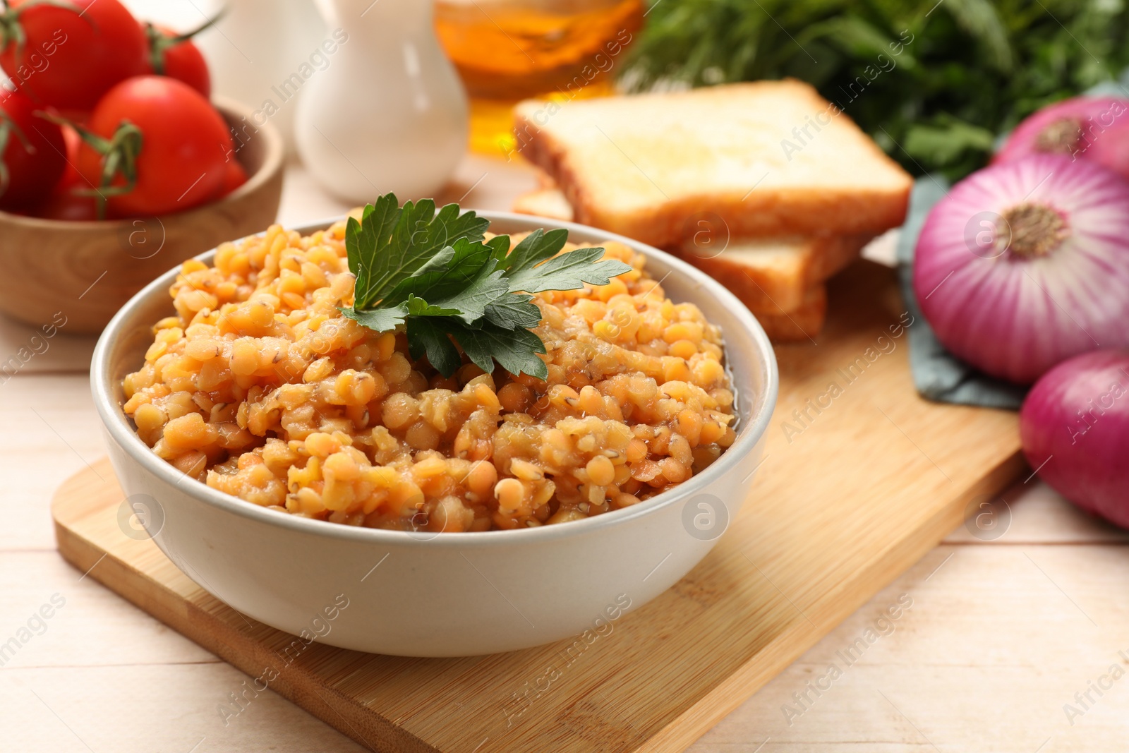 Photo of Delicious red lentils with parsley in bowl served on table, closeup