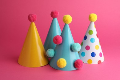 Photo of Beautiful party hats with pompoms on pink background