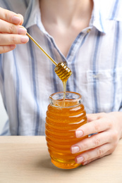 Woman with jar of honey at wooden table, closeup