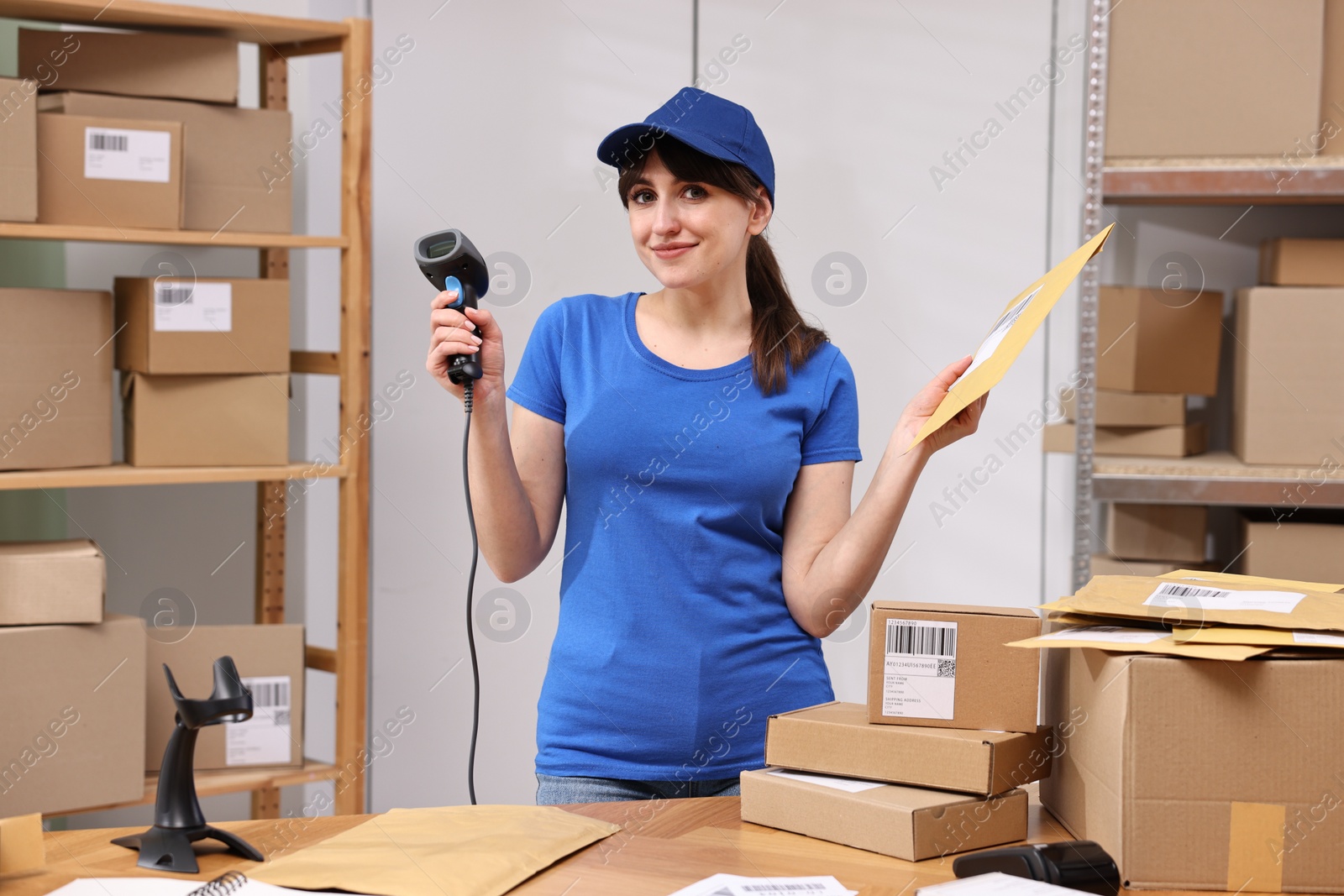 Photo of Parcel packing. Post office worker with barcode scanner and bag at wooden table indoors