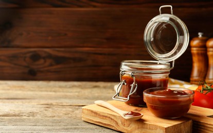 Tasty barbeque sauce in bowl, jar and spoon on wooden table, closeup. Space for text