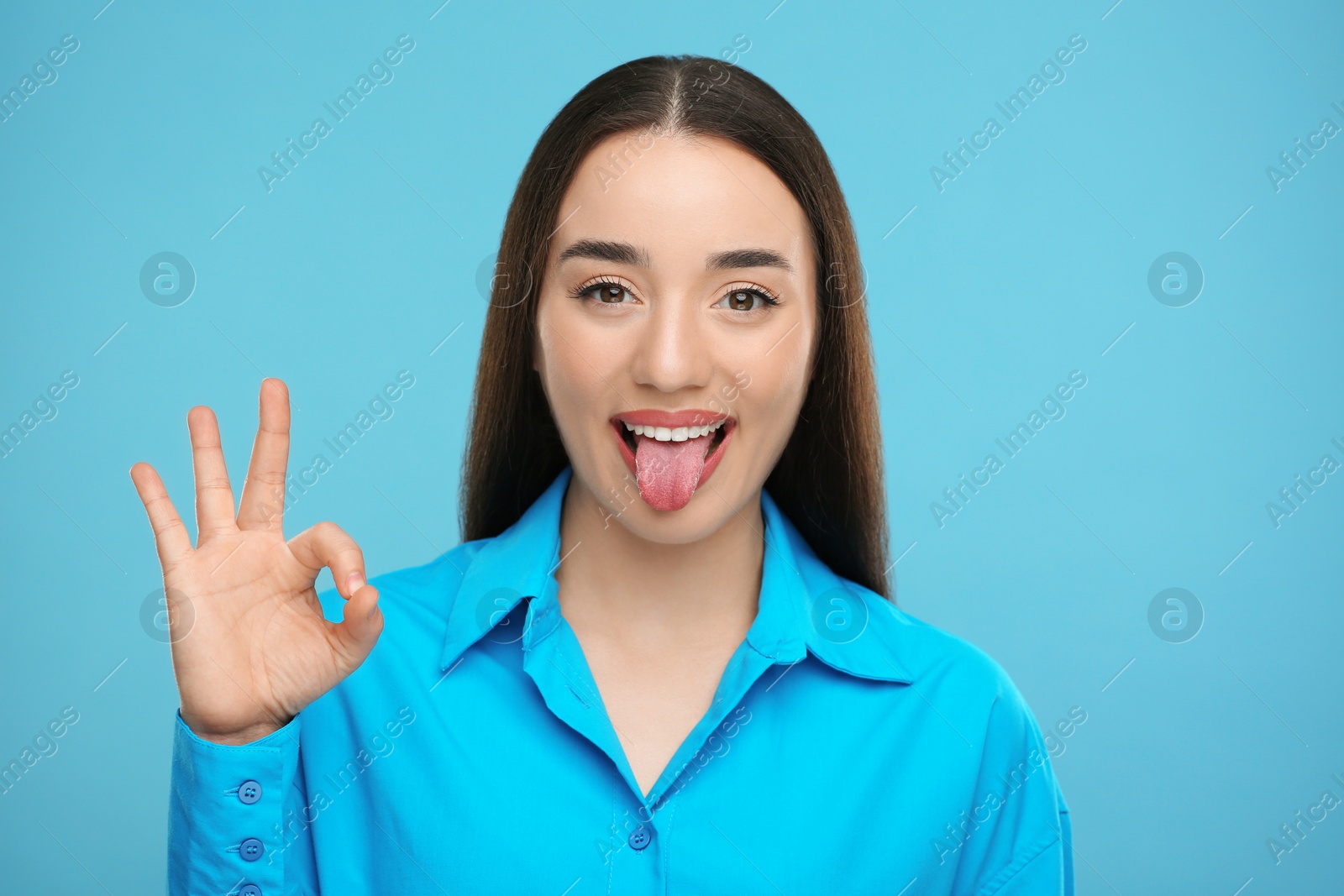 Photo of Happy woman showing her tongue and OK gesture on light blue background