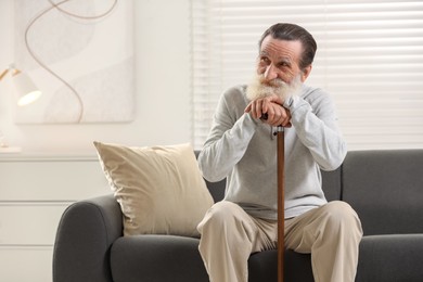 Photo of Senior man with walking cane on sofa at home