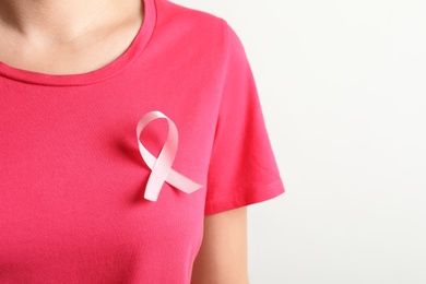 Photo of Woman with pink ribbon on t-shirt against light background. Cancer awareness
