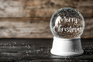 Image of Beautiful snow globe with phrase Merry Christmas on wooden table. Space for text