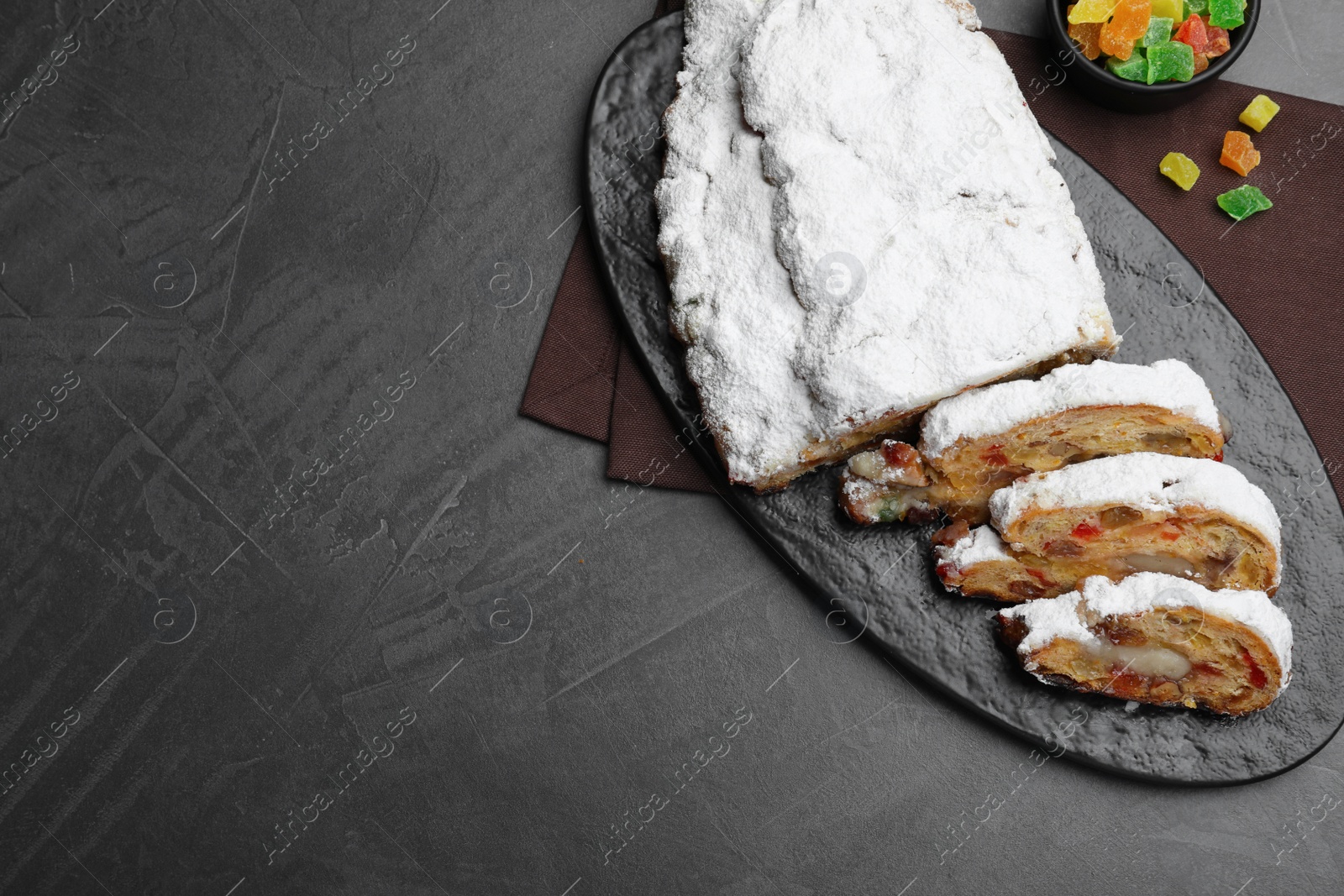 Photo of Traditional Christmas Stollen with icing sugar on black table, flat lay. Space for text