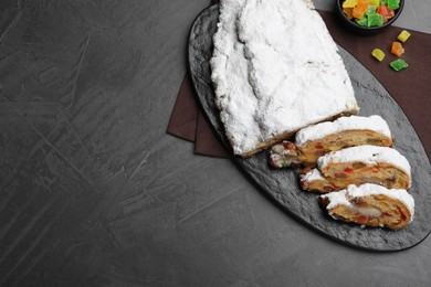 Traditional Christmas Stollen with icing sugar on black table, flat lay. Space for text