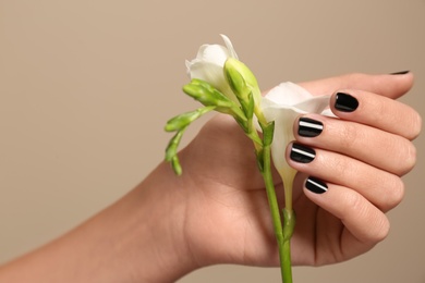 Photo of Woman with black manicure holding flower on color background, closeup. Nail polish trends