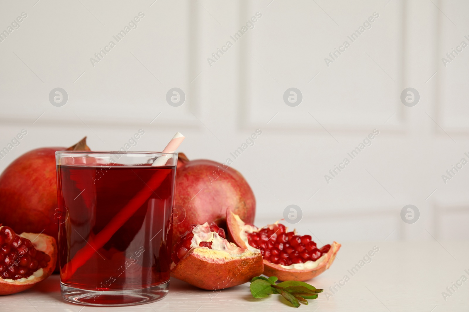 Photo of Glass of pomegranate juice and fresh fruits on white table, space for text